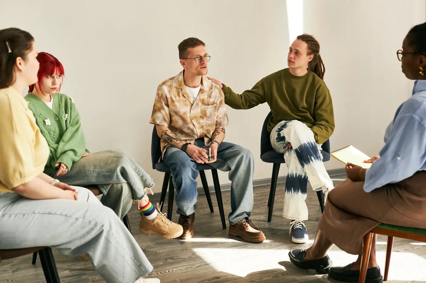 Adults gathered in a bright room sharing a quiet moment of connection, listening to one another