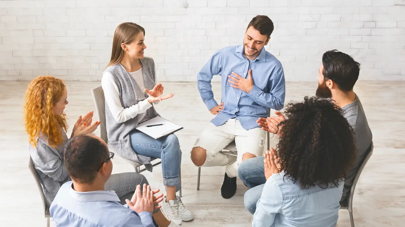 Adults seated around a bright, sunlit room sharing a moment of connection during a group session